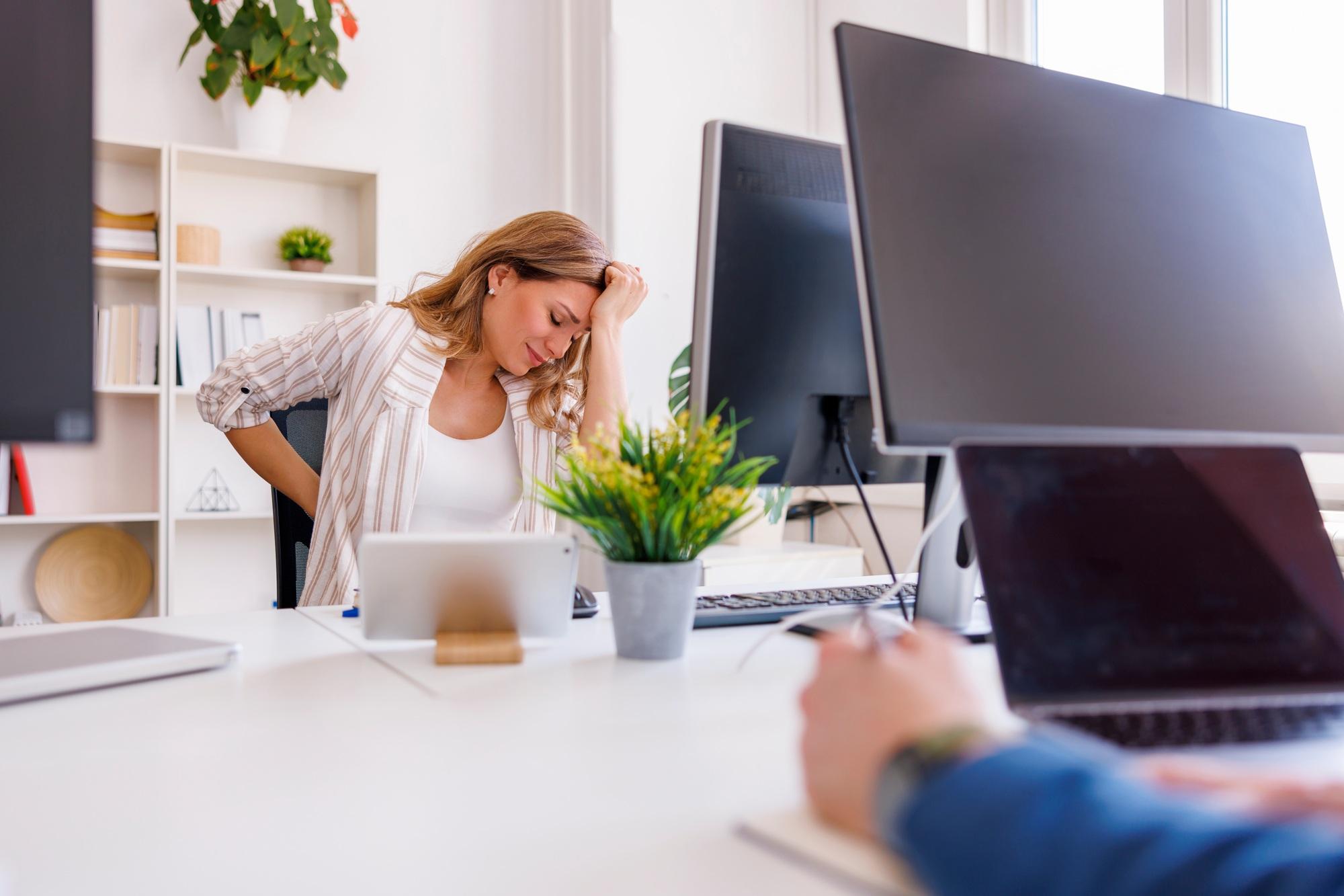 Business woman having backpain and headache while working in an office